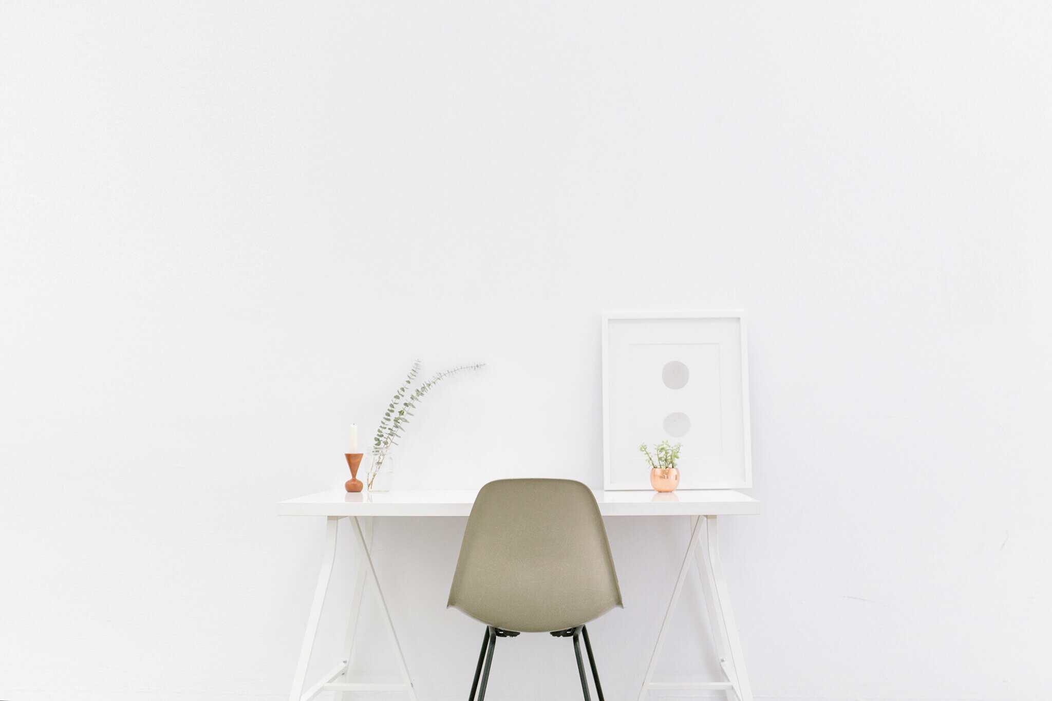 White desk with a green chair, minimalist decor, and potted plants in a bright, modern workspace.