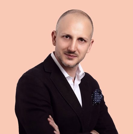 Professional portrait of a confident businessman Nodvik CEO in a black suit against a peach background.